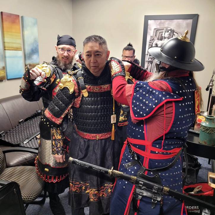 John Cosma, left,  and Terri G, right, help Johnny Wu into his armor.